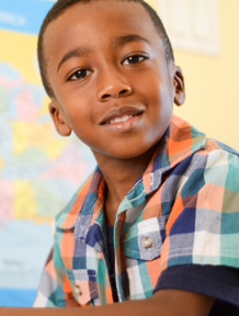 kid in plaid shirt in classroom in front of map